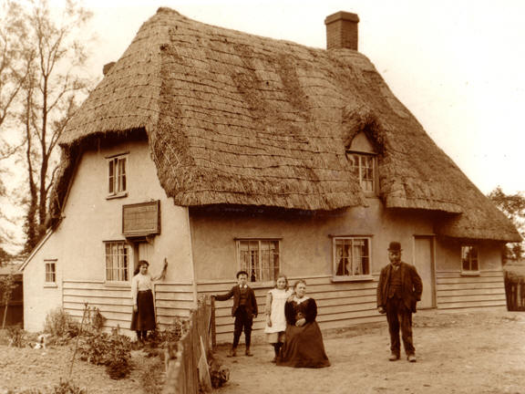 The Coopers at Abbess Roding. The people in the photograph are John Blowes, his wife, Ada, and three of their children - (left to right) Julia, Francis (known as Dick), and Margaret. You can just make out the name John Blowes on the board on the end of the building.